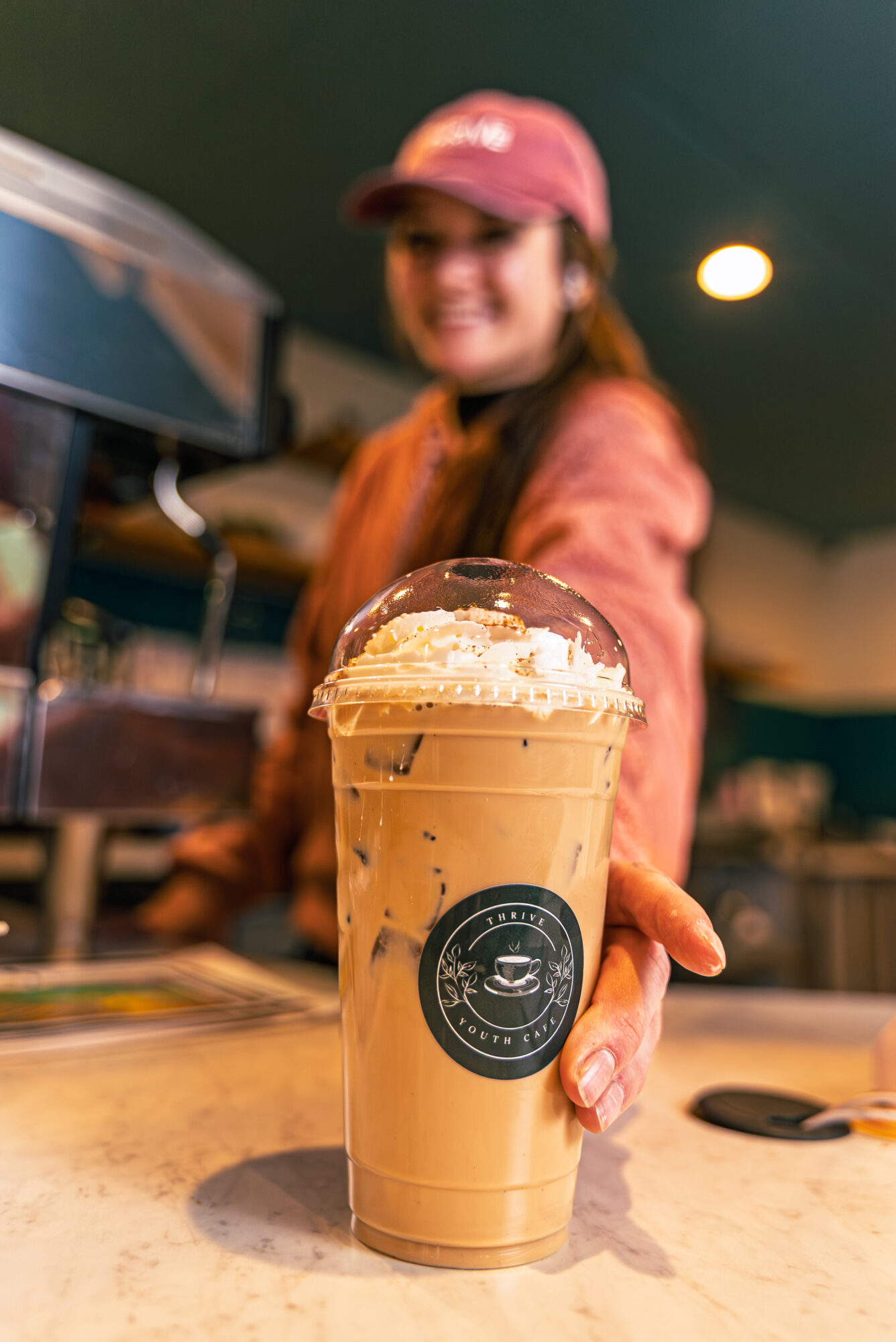 Smiling barista offers iced coffee at cafe.