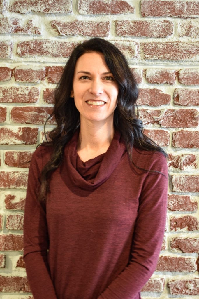 Woman smiling in front of brick wall.