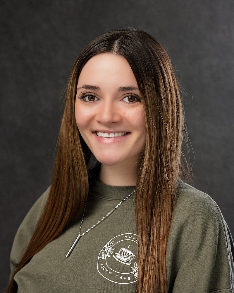 Smiling person in green sweater with cafe logo.