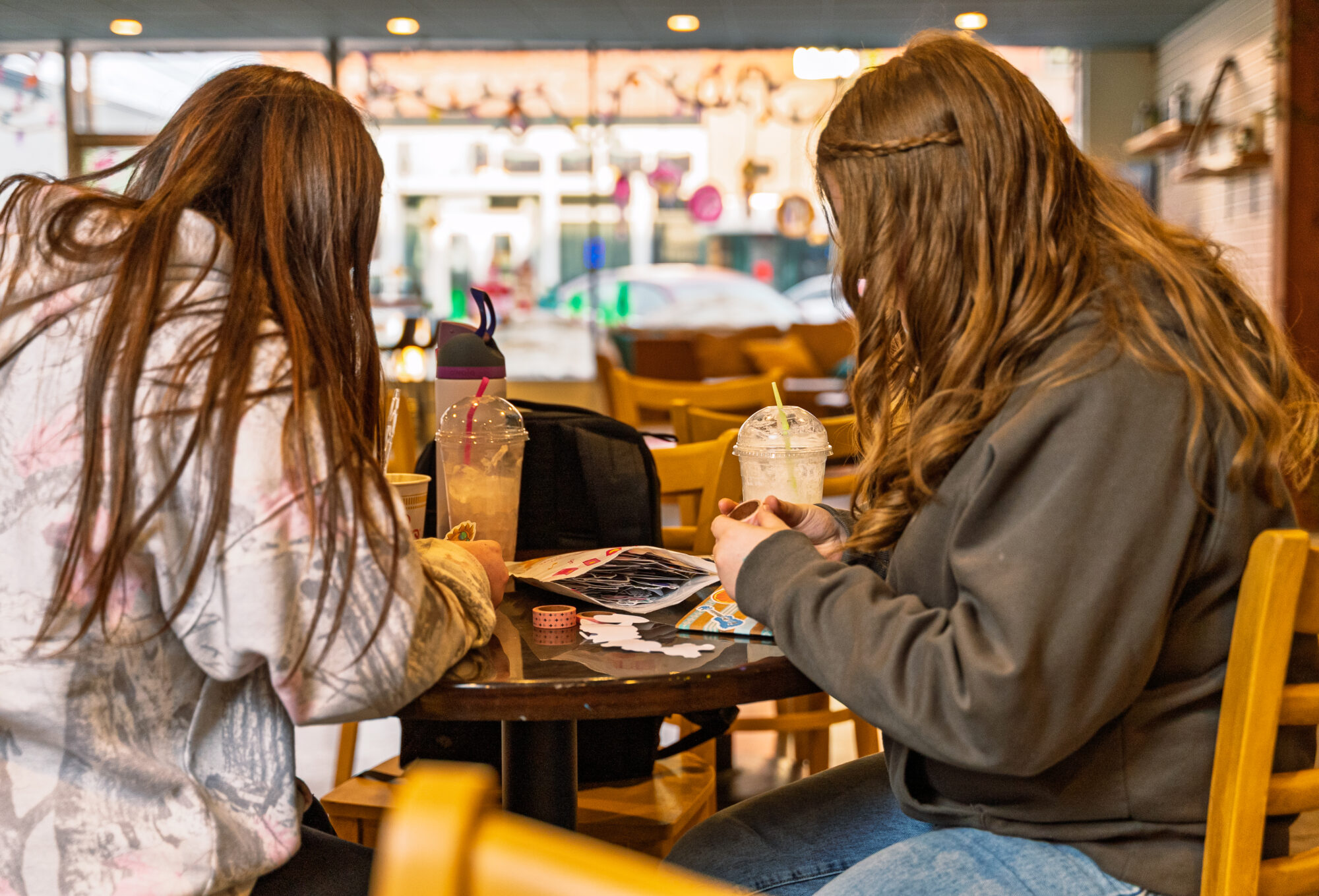 Two people crafting with drinks at a cafe.