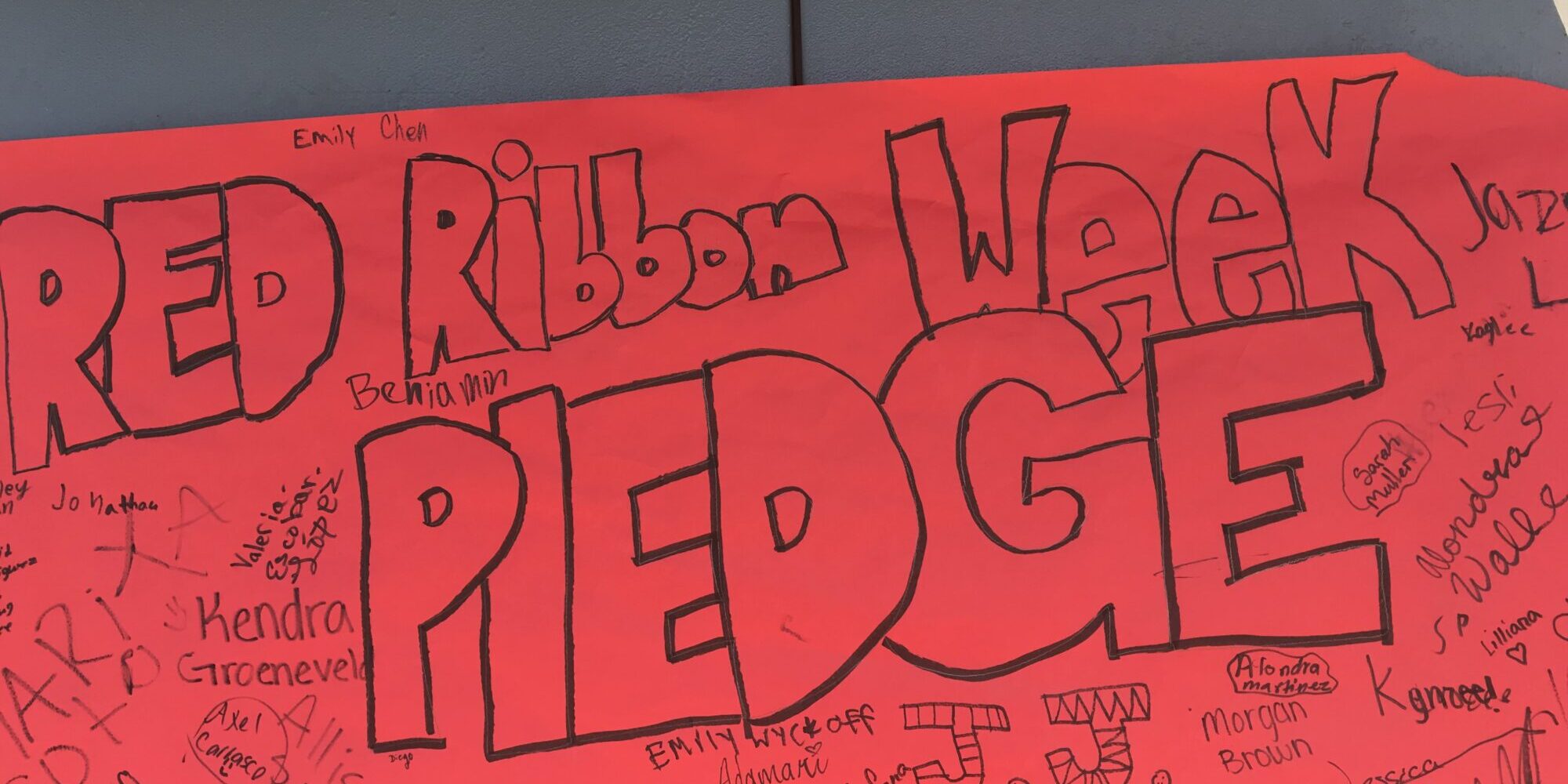 Red Ribbon Week pledge with signatures on red poster.
